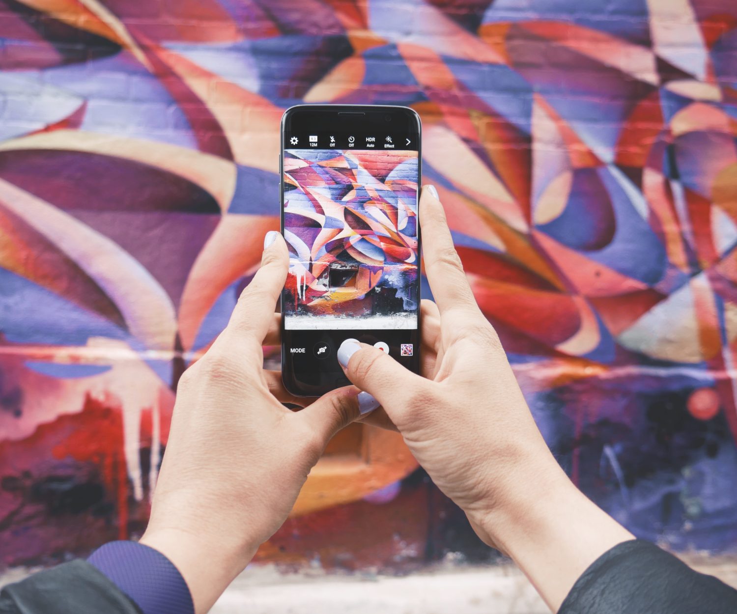 An Instagrammer with a phone taking a photo of a mural