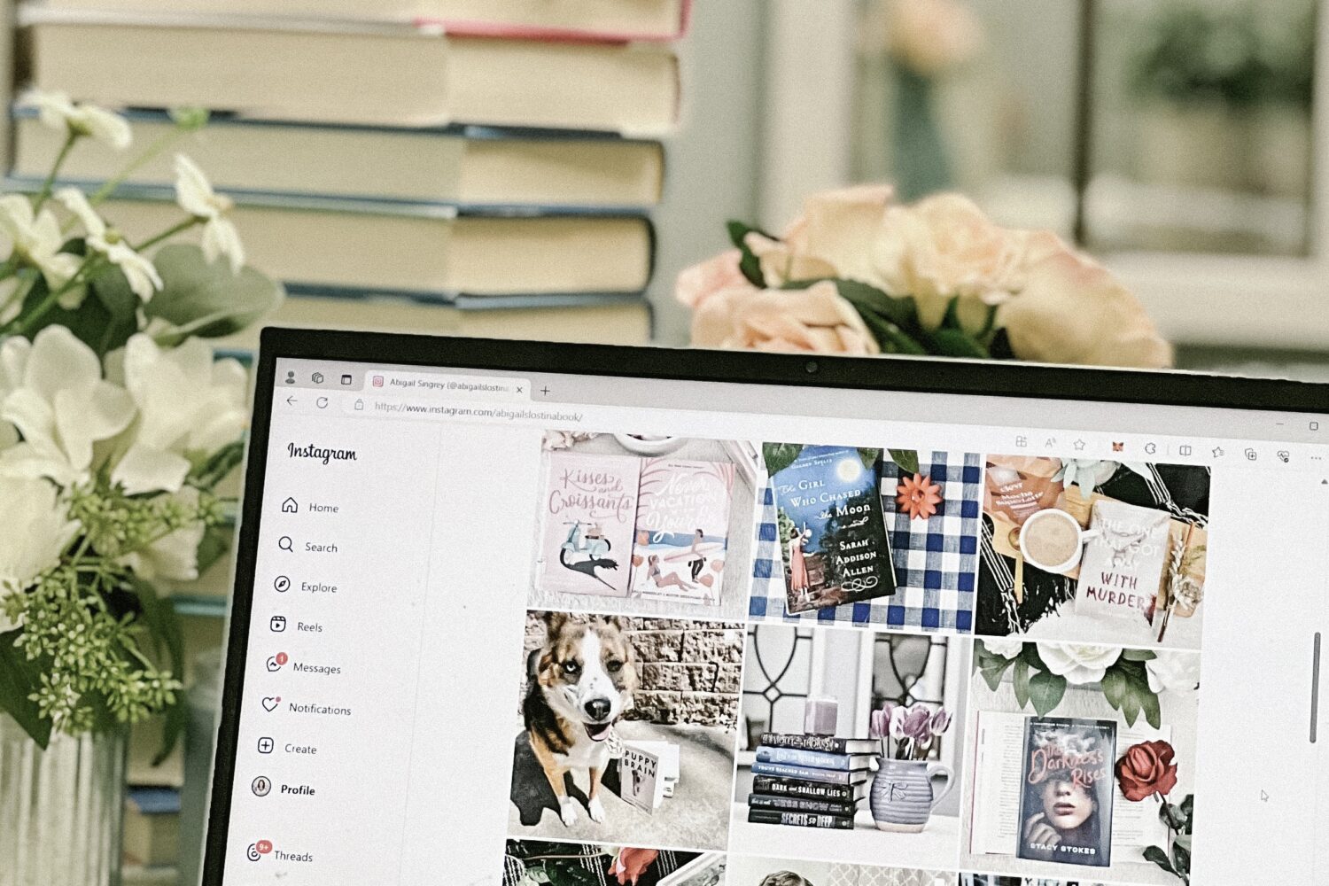 A laptop displaying a bookstagram account in front of a pile of books.